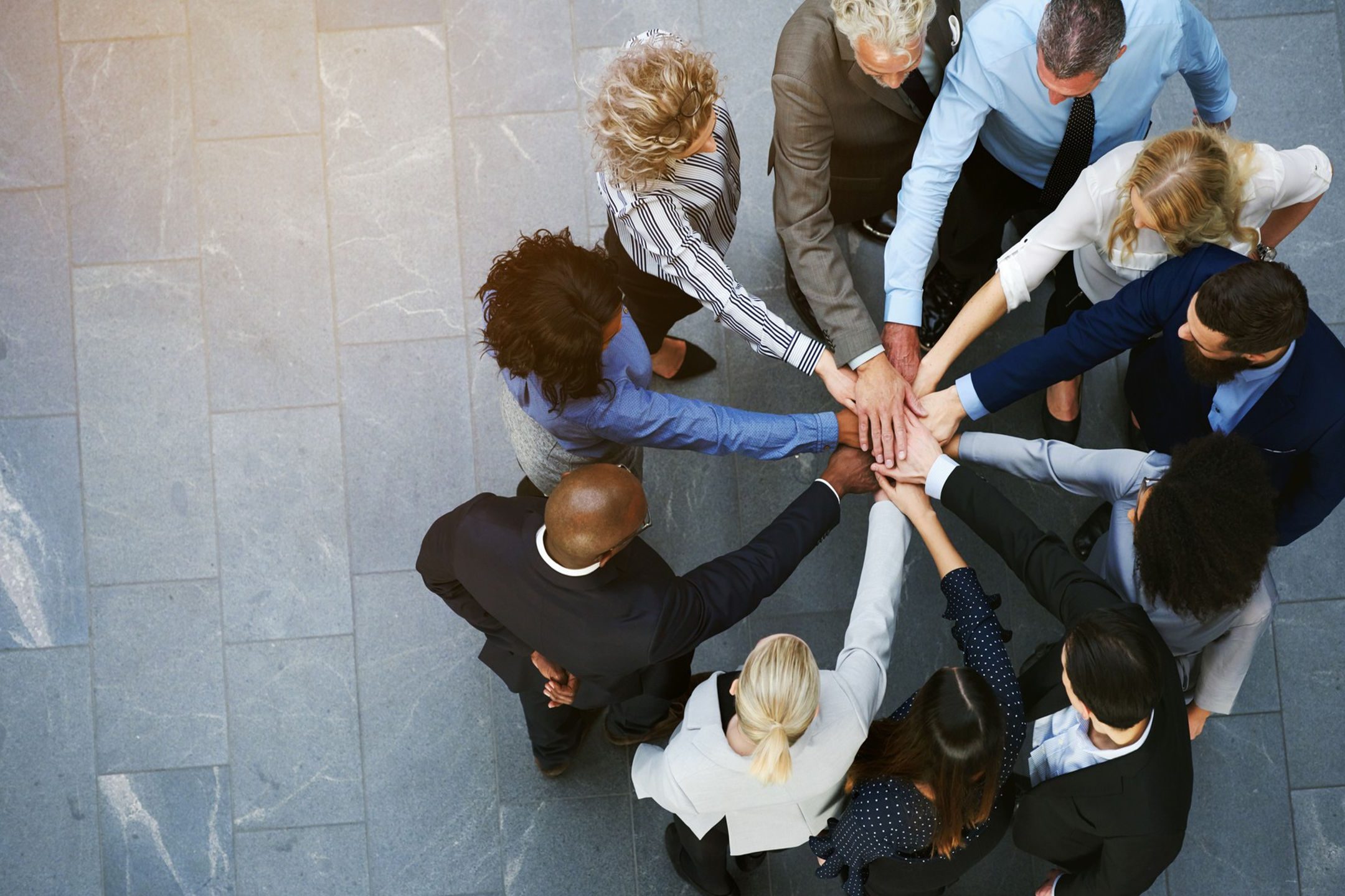 A diverse group joining hands in a teamwork gesture from above.