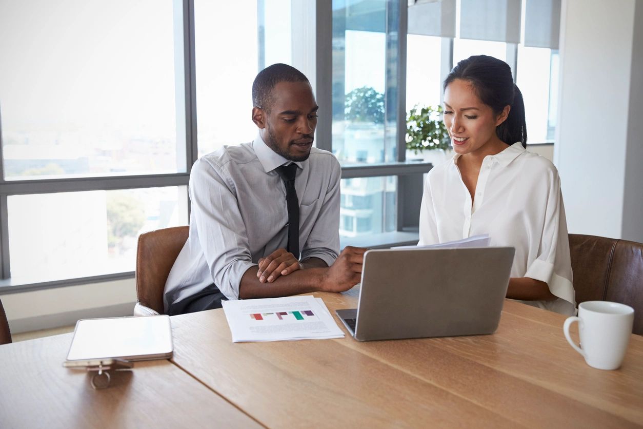 Two colleagues discussing business data on a laptop in an office.