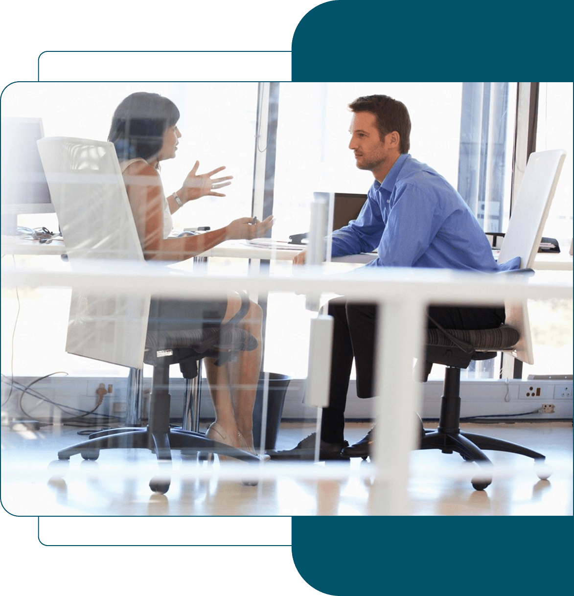 Two professionals discussing work across a glass office table.